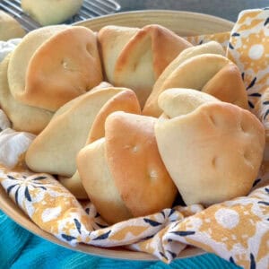 8 coco bread rolls in a basket lined with a flowery cloth napkin.
