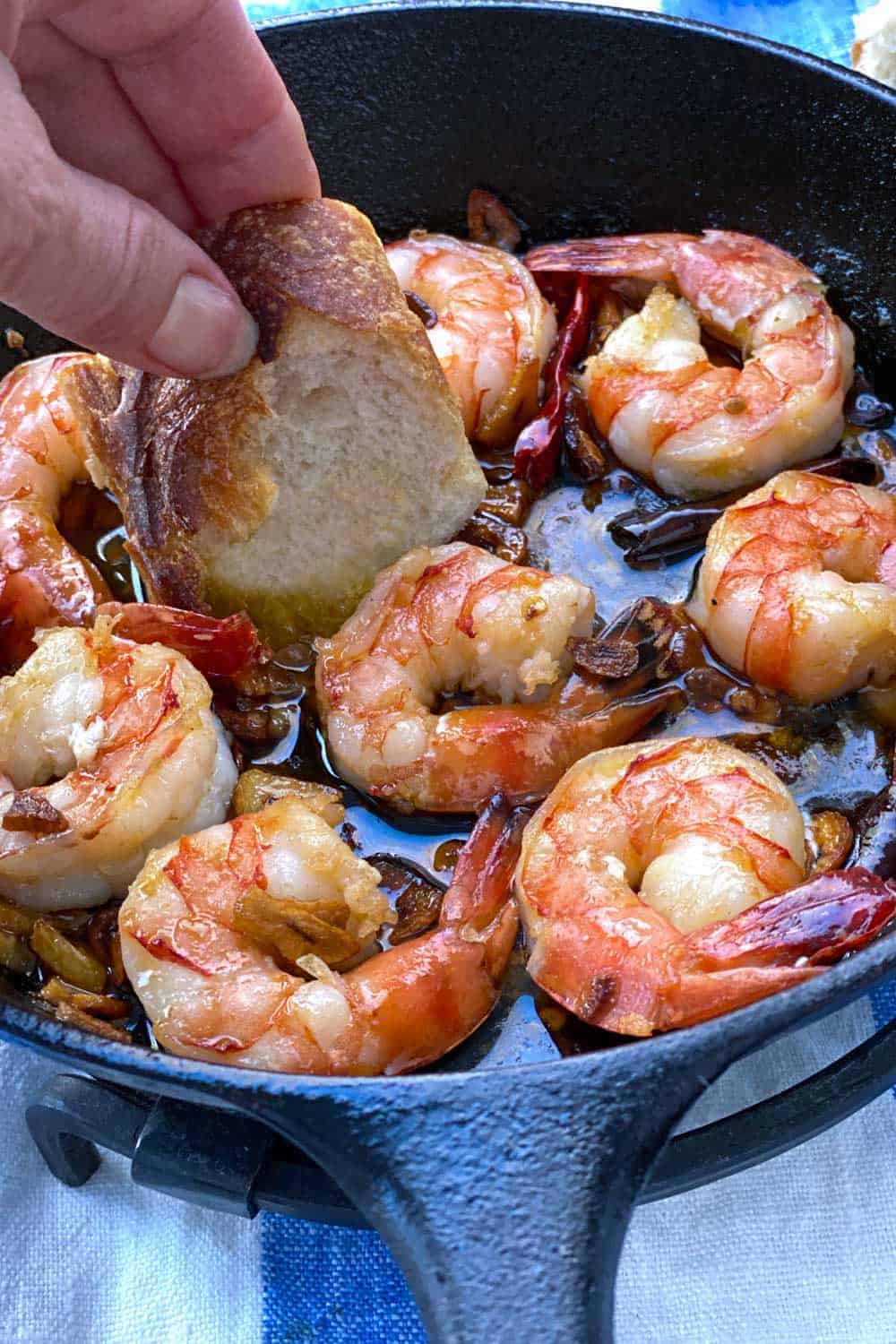 8 shrimp in a skillet with bread being dipped into the garlicky oil