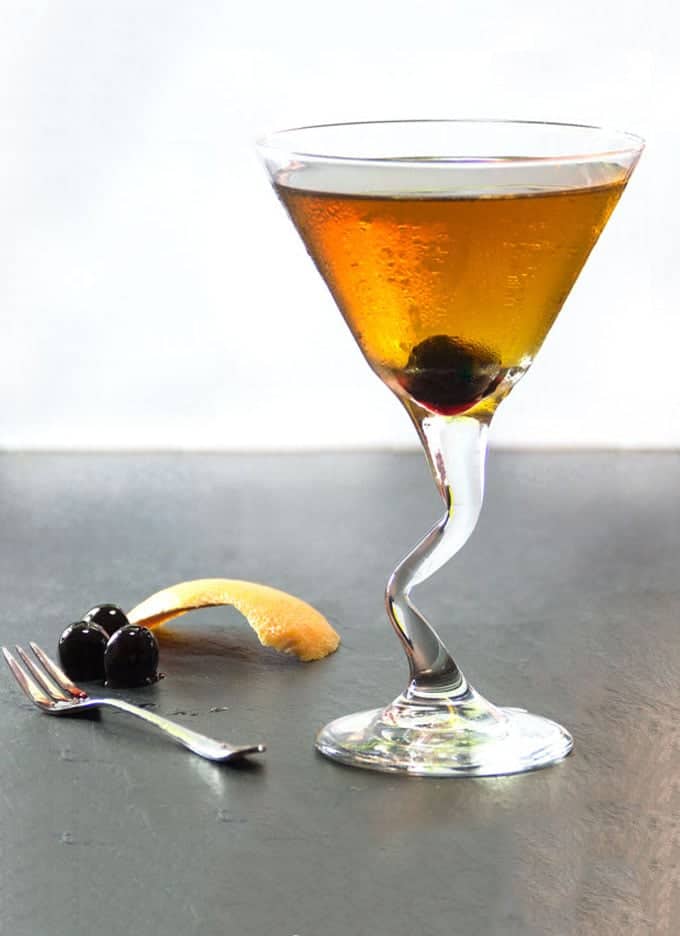 Perfect Manhattan cocktail in a martini glass with a piece of orange zest on the counter and a cherry
