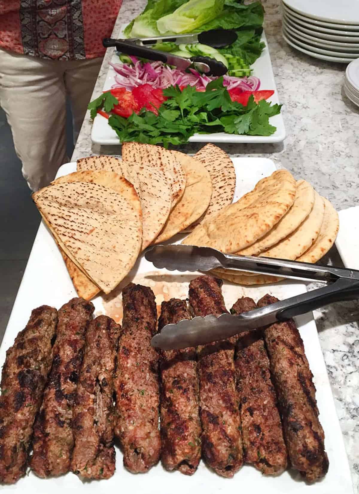Buffet set up with a platter of 8 lamb kofta kebabs, toasted pitas, lettuce, tomatoes and parsley.