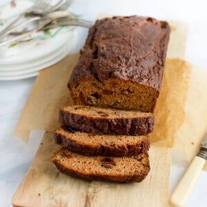 A loaf of pumpkin bread on a wooden board with three slices cut and leaning down from the loaf.