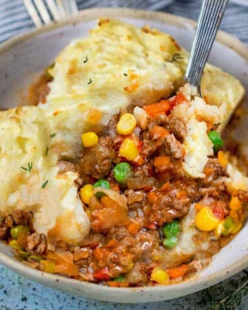 bowl of cooked ground beef with corn and peas in sauce topped with fluffy mashed potatoes.