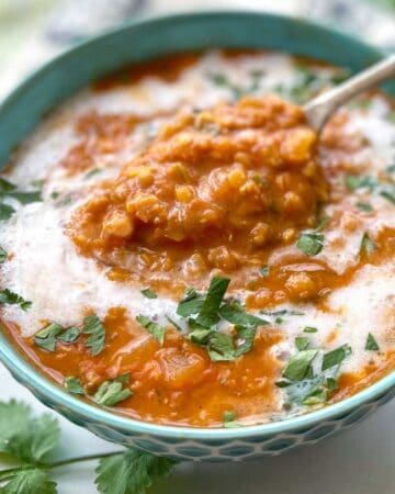 blue bowl filled with red lentil soup drizzled with coconut milk and sprinkled with chopped cilantro