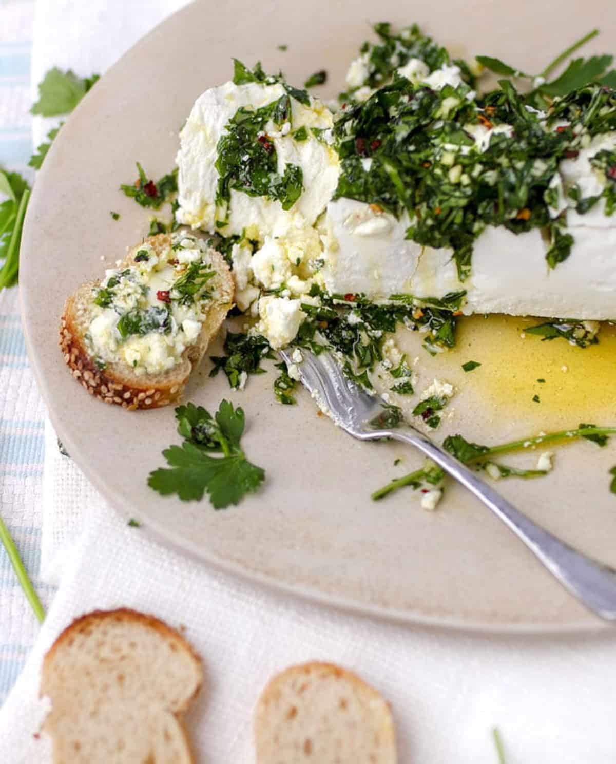 Log of goat cheese topped with parsley and olive oil, on a platter