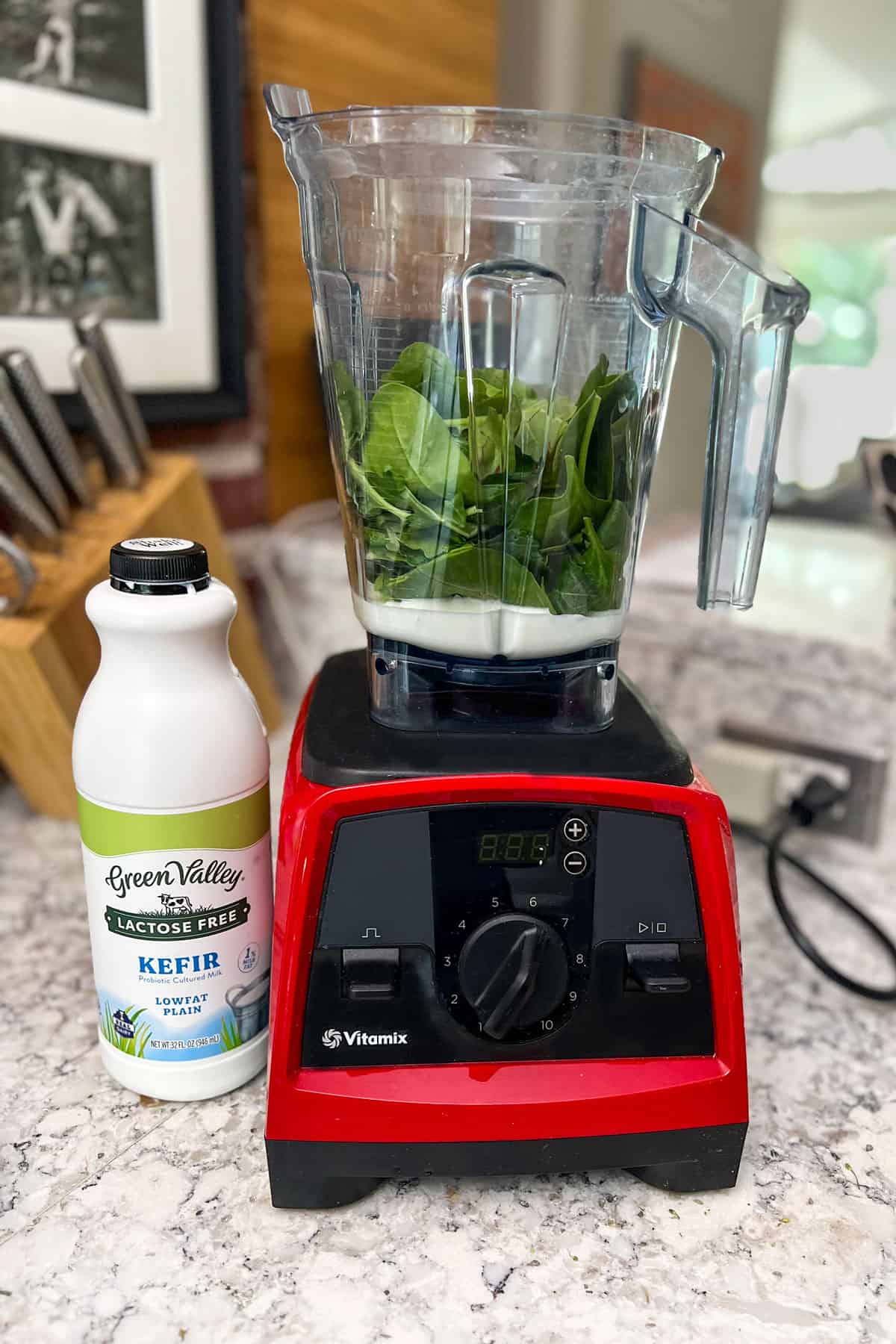 Vitamix blender with kefir and kale leave in the blending container, and a bottle of kefir on the counter next to it.