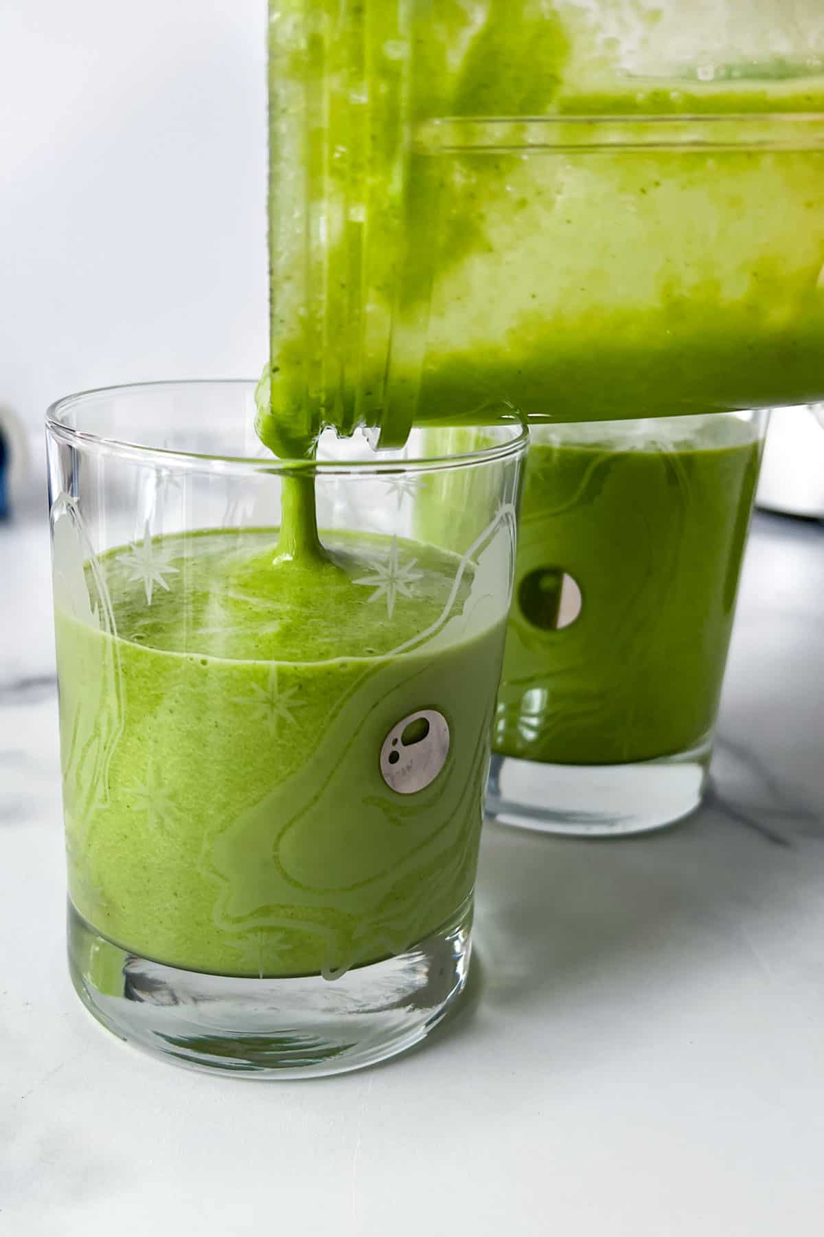 Vivid green smoothie being poured from a plastic blender cup into a glass.